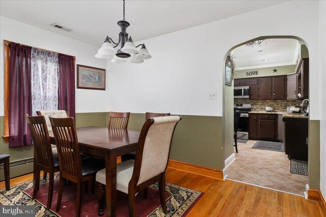 dining area with an inviting chandelier, arched walkways, light wood-type flooring, visible vents, and baseboards