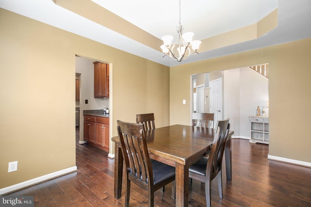 dining area with a tray ceiling, a notable chandelier, dark wood-style flooring, and baseboards