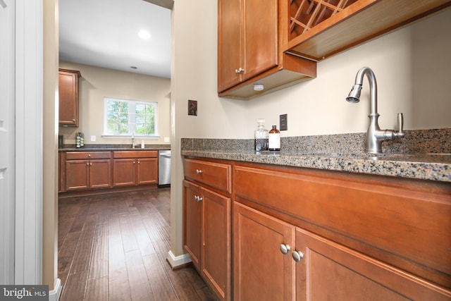kitchen with dark stone countertops, dark wood-style flooring, a sink, dishwasher, and brown cabinets