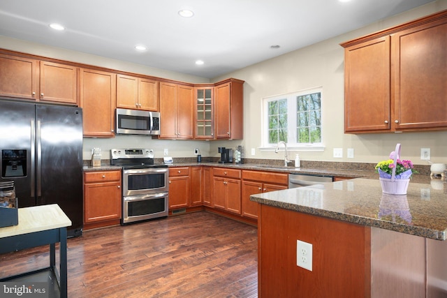 kitchen with a peninsula, brown cabinets, dark wood finished floors, stainless steel appliances, and a sink