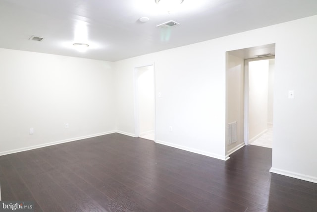 empty room featuring baseboards, visible vents, and dark wood-style flooring