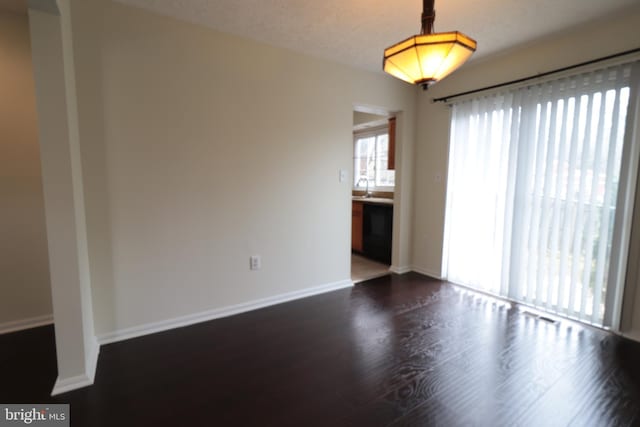 empty room with baseboards, a sink, and dark wood finished floors