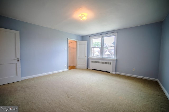 unfurnished bedroom featuring a closet, baseboards, radiator, a spacious closet, and carpet floors
