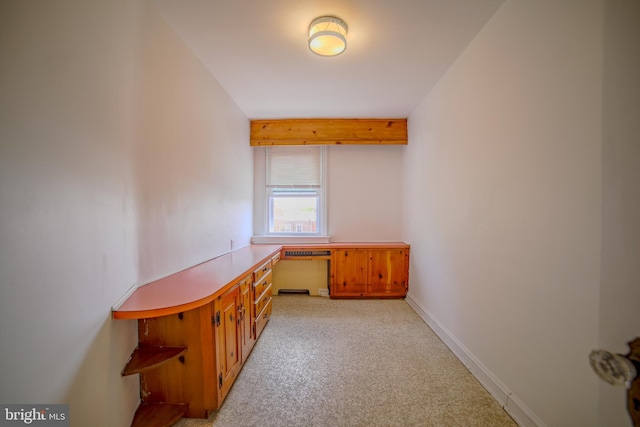 unfurnished office with built in study area, light colored carpet, beamed ceiling, and baseboards