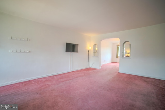 spare room featuring arched walkways, baseboards, and carpet