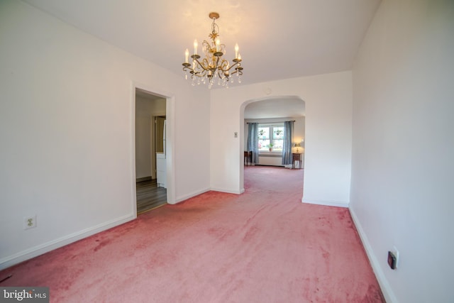 unfurnished room with an inviting chandelier, arched walkways, baseboards, and carpet floors