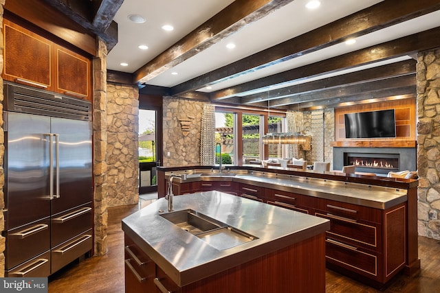 kitchen with stainless steel built in fridge, a large island with sink, beam ceiling, and stainless steel countertops