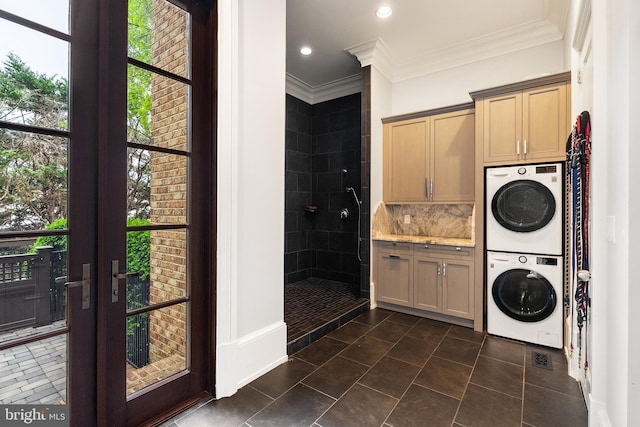 laundry area featuring cabinet space, stacked washing maching and dryer, dark tile patterned flooring, ornamental molding, and recessed lighting