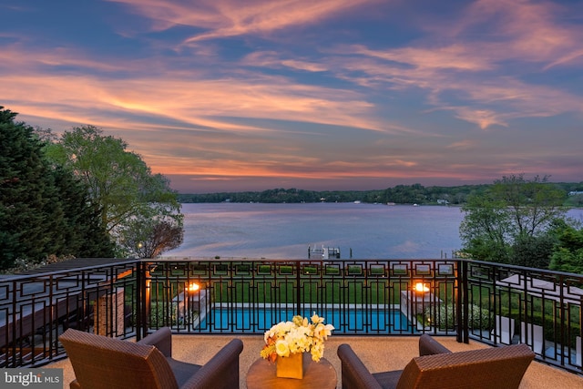 balcony at dusk featuring a water view