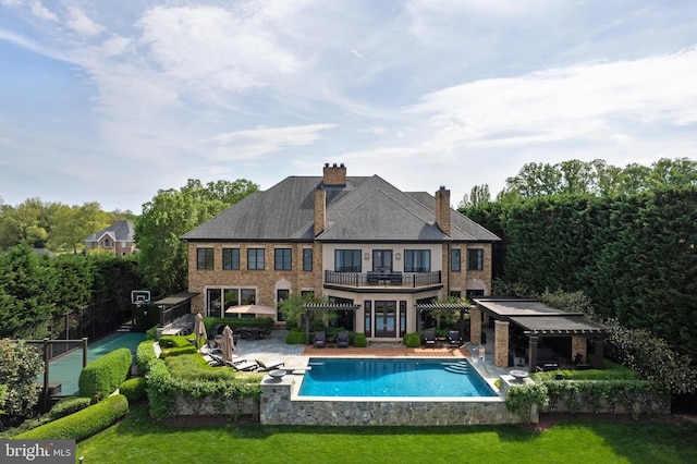 back of property with an outdoor pool, a chimney, a balcony, a lawn, and a patio