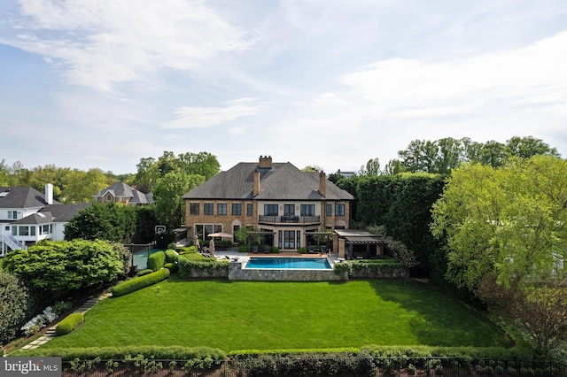 rear view of house featuring a lawn, a chimney, an outdoor pool, and a balcony