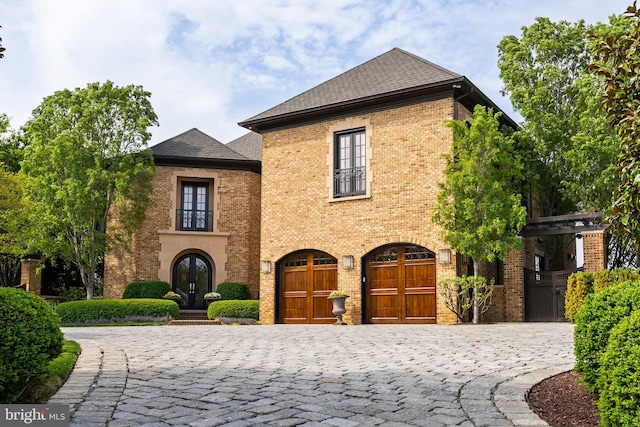 view of front of property with a garage, curved driveway, roof with shingles, french doors, and brick siding