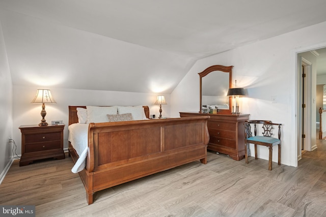 bedroom with vaulted ceiling, baseboards, and light wood-style floors