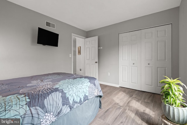 bedroom featuring baseboards, wood finished floors, visible vents, and a closet