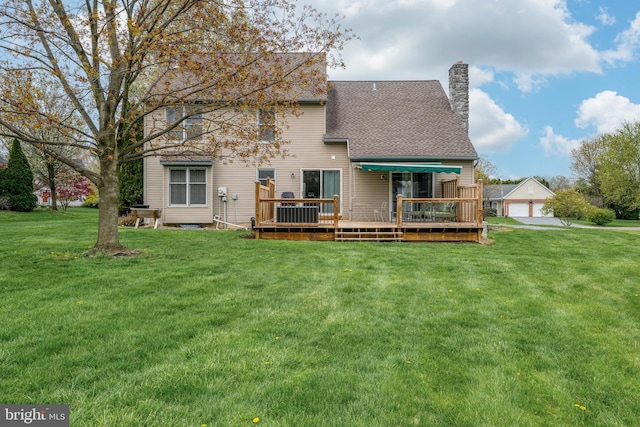 rear view of property featuring roof with shingles, a detached garage, a chimney, a wooden deck, and a yard