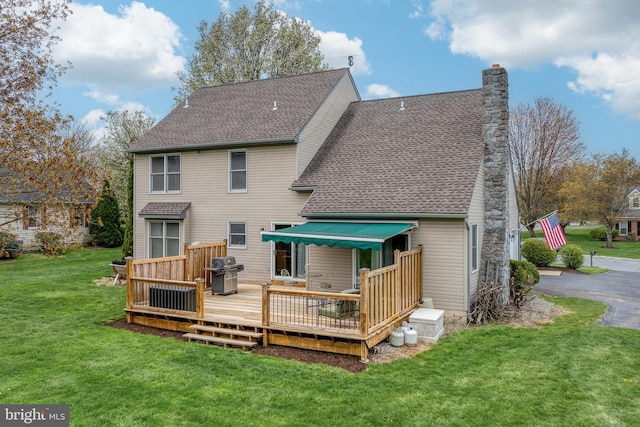 rear view of house featuring a lawn, a chimney, roof with shingles, and a deck