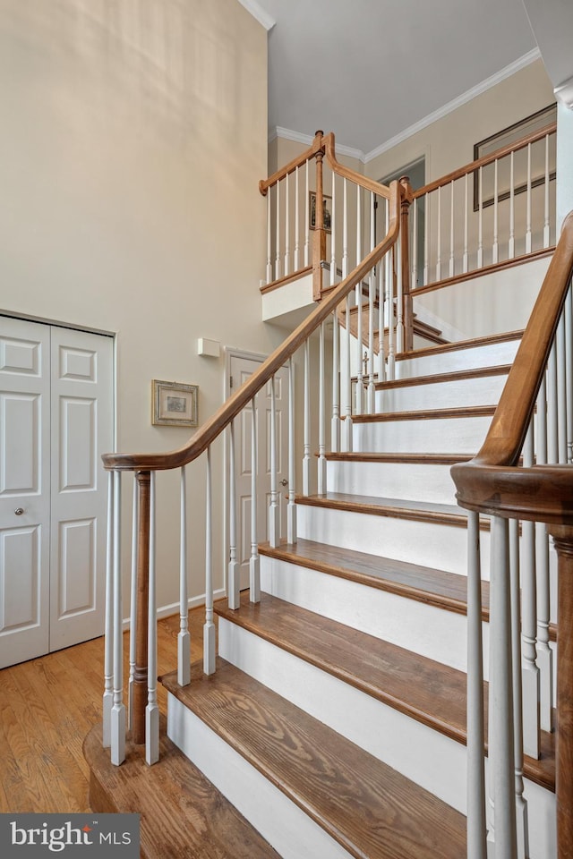 stairs with a towering ceiling, wood finished floors, and crown molding