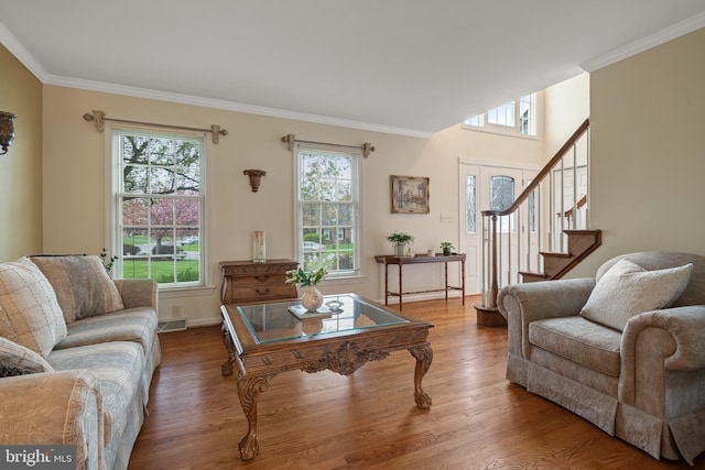 living area featuring wood finished floors, crown molding, baseboards, and stairway