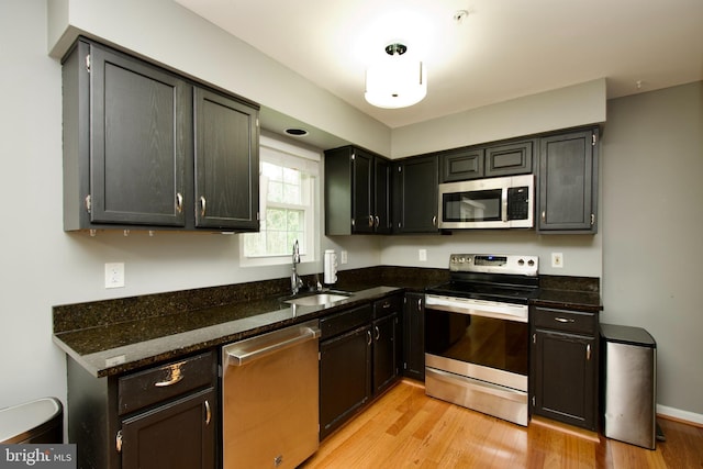kitchen with stainless steel appliances, a sink, light wood-style flooring, and dark stone countertops
