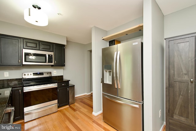 kitchen featuring dark stone counters, stainless steel appliances, baseboards, and light wood-style floors