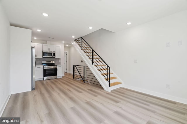 unfurnished living room with baseboards, recessed lighting, light wood-style flooring, and stairway