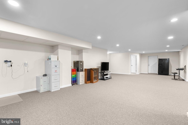 finished below grade area featuring baseboards, recessed lighting, light colored carpet, and black fridge with ice dispenser