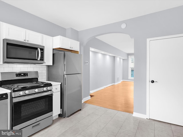 kitchen with light countertops, decorative backsplash, arched walkways, white cabinets, and appliances with stainless steel finishes