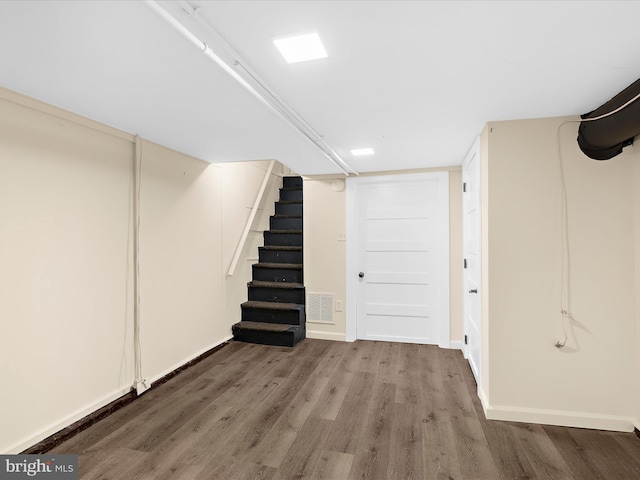 finished below grade area with baseboards, visible vents, stairway, and wood finished floors
