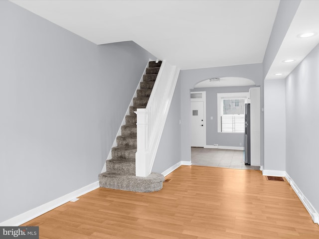 foyer entrance featuring stairway, light wood-type flooring, baseboards, visible vents, and arched walkways