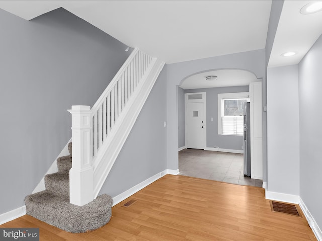 foyer entrance with arched walkways, baseboards, light wood-style floors, and visible vents