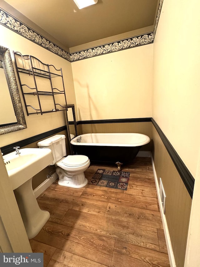 full bath with toilet, a wainscoted wall, visible vents, a freestanding bath, and wood finished floors