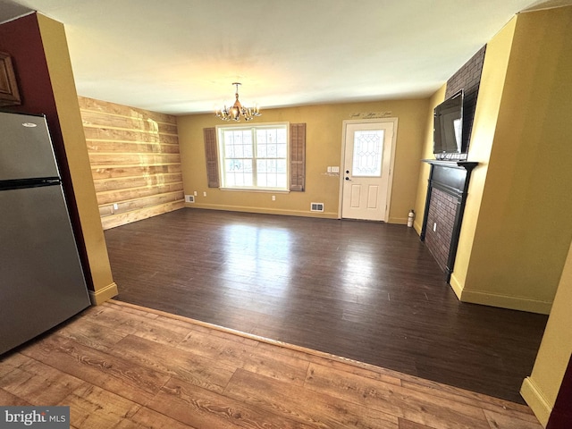 unfurnished dining area with wood walls, visible vents, a notable chandelier, a fireplace, and wood finished floors
