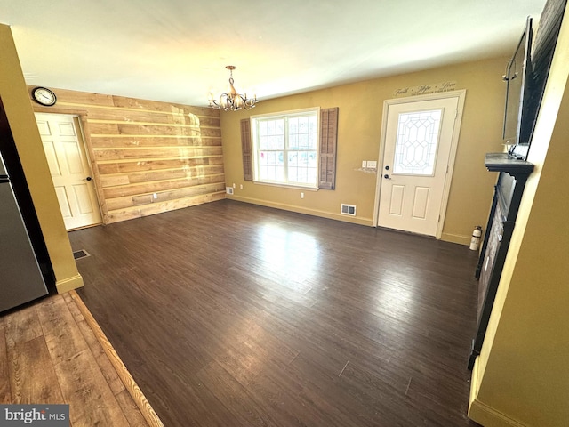 unfurnished dining area with dark wood-style flooring, visible vents, an inviting chandelier, and wood walls