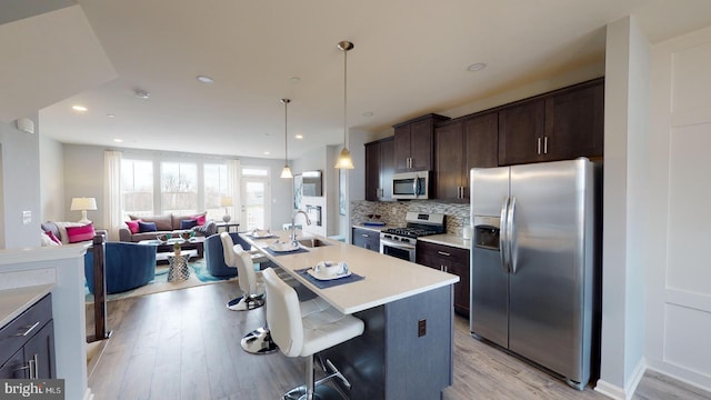 kitchen featuring decorative backsplash, light countertops, dark brown cabinets, appliances with stainless steel finishes, and a sink