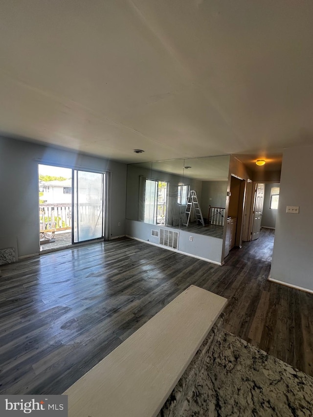 unfurnished living room featuring dark wood finished floors, visible vents, baseboards, and a healthy amount of sunlight