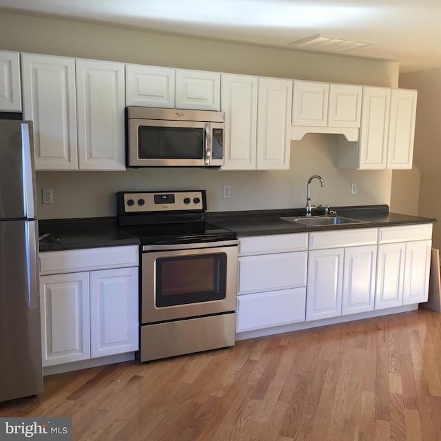 6549 Locust Grove Rd, Easton, MD 21601 - kitchen with stainless steel appliances, a sink, dark countertops, white cabinets, and light wood finished floors