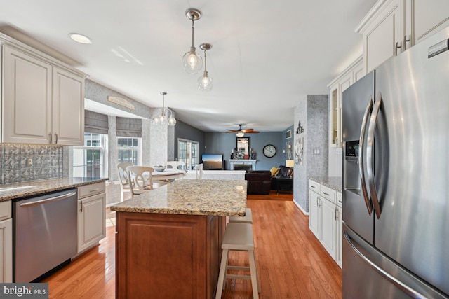 kitchen featuring ceiling fan, light wood-style flooring, a center island, appliances with stainless steel finishes, and a breakfast bar area