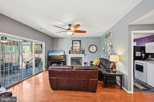 living room with baseboards, light wood-style floors, ceiling fan, a high end fireplace, and washing machine and clothes dryer