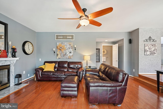living area featuring wood finished floors, a high end fireplace, a ceiling fan, and baseboards