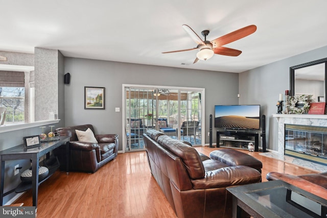 living room with ceiling fan, a premium fireplace, wood finished floors, and baseboards