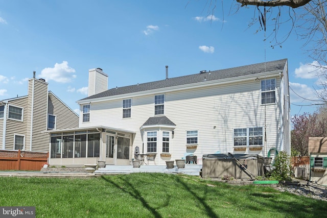 back of house featuring a chimney, a sunroom, a hot tub, fence, and a lawn