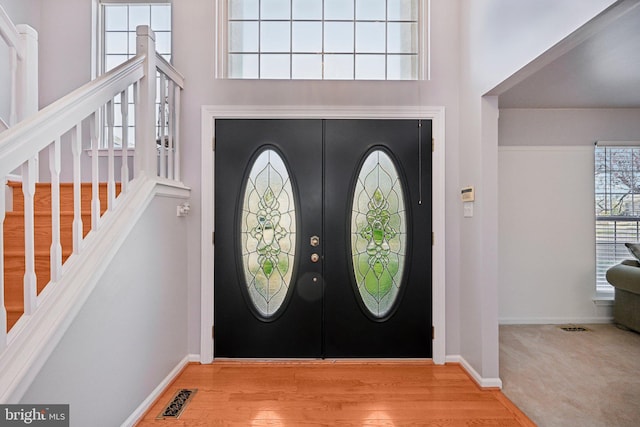 entryway with wood finished floors, baseboards, visible vents, and stairway