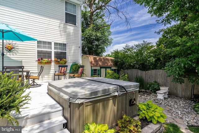 wooden terrace with an outbuilding, fence, a storage unit, and a hot tub