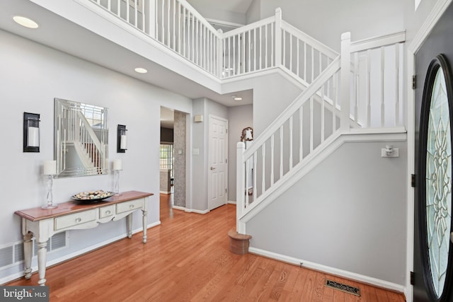 entryway with baseboards, stairway, a high ceiling, visible vents, and wood finished floors