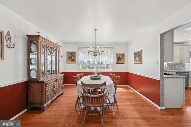 dining space featuring baseboards, light wood-type flooring, and a notable chandelier