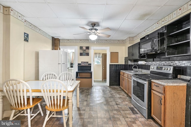 kitchen with a sink, freestanding refrigerator, black microwave, stainless steel range with electric stovetop, and brown cabinets