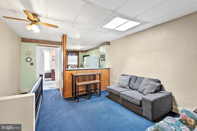 living area with carpet floors, ceiling fan, and a drop ceiling