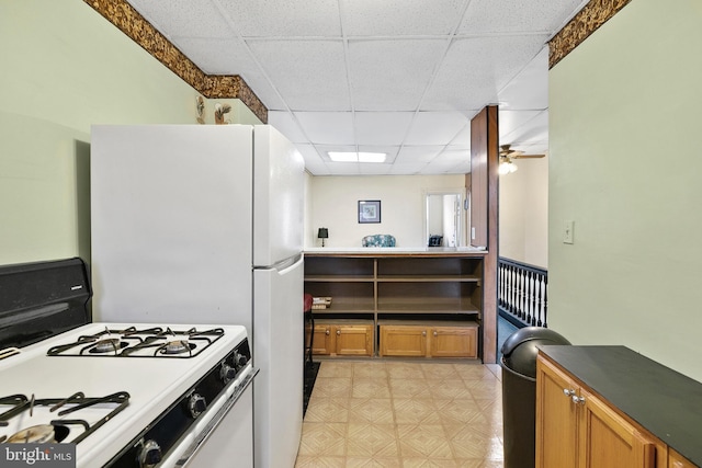 kitchen with a paneled ceiling, white range with gas stovetop, brown cabinetry, and light floors