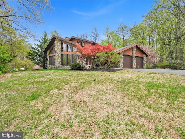 mid-century inspired home with a front yard, driveway, an attached garage, and stone siding