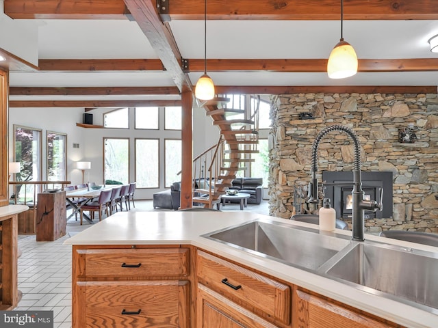 kitchen featuring pendant lighting, a wood stove, beam ceiling, light countertops, and a sink